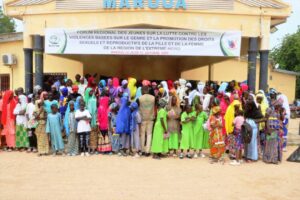 Un grand groupe d'activistes, principalement des jeunes filles et des adolescentes, se tient ensemble devant un bâtiment avec une pancarte affichant le nom du forum : "Forum Régional des Jeunes sur la Lutte Contre les Violences Basées sur le Genre et la Promotion des Droits Sexuels et Reproductifs de la Fille et de la Femme de la Région de l'Extrême-Nord". Les participants se sont réunis pour sensibiliser à la violence sexuelle et basée sur le genre.