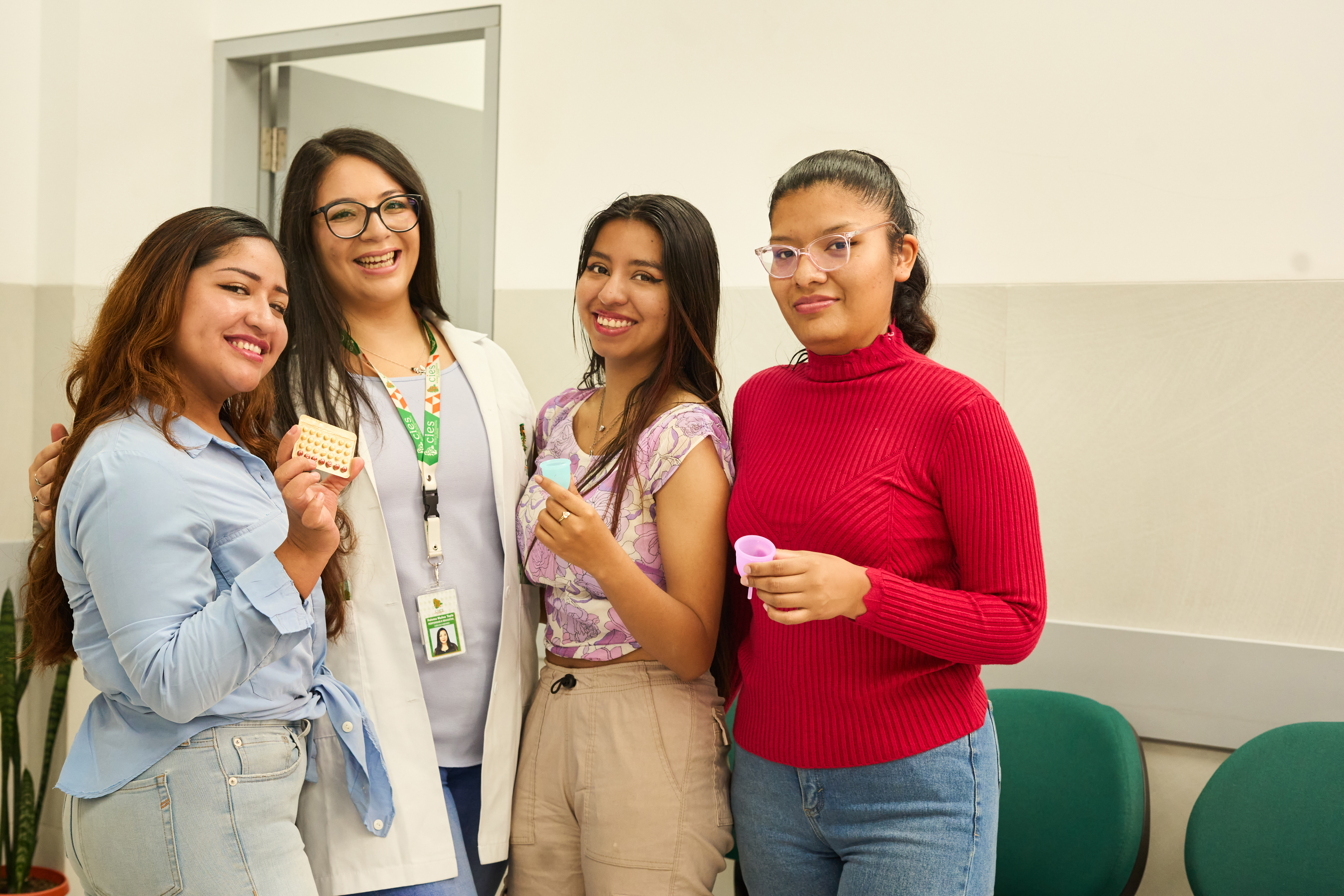 A CIES health worker in Bolivia stands with three clients, each holding contraceptive pills or menstrual cups.
